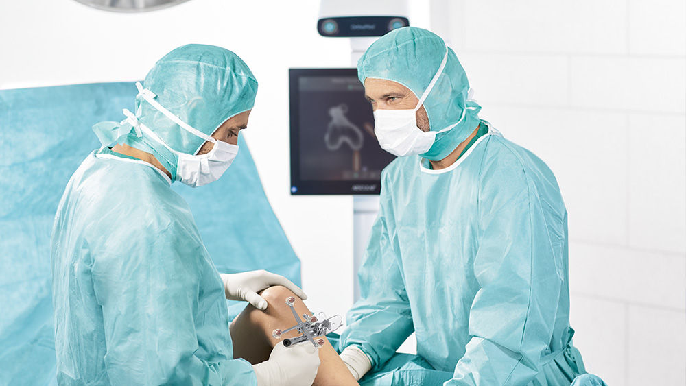 Dwóch chirurgów za pomocą narzędzia OrthoPilot® Elite Multitool i monitora w tle