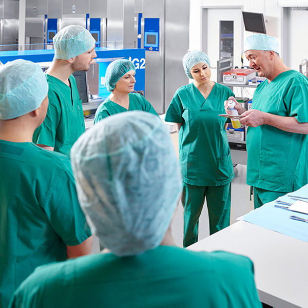 Jeden z lekarzy pokazuje coś kilku lekarzom i pielęgniarkom chirurgicznym znajdującym się na sali operacyjnej