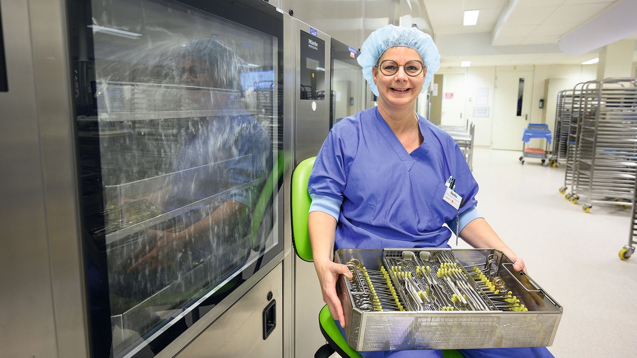 Uśmiechnięta pielęgniarka siedzi na krześle z zestawem narzędzi, jest wyposażona w nasadkę higieniczną