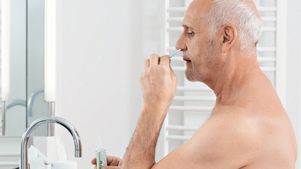 starszy mężczyzna wykonujący przeciwdrobnoustrojowe płukanie nosa w domu przed lustrem kąpielowym 