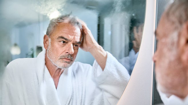 starszy mężczyzna w szlafroku zastanawia się nad zaparowanym lustrem łazienkowym