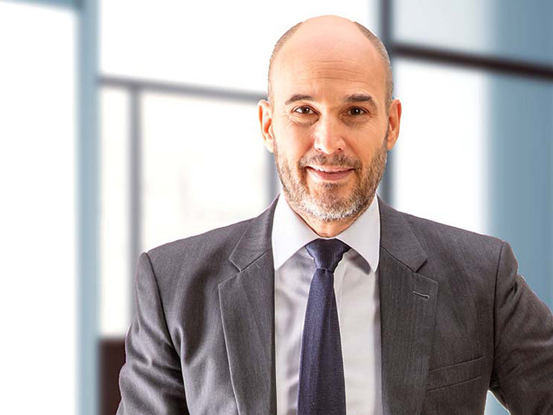 Mężczyzna w garniturze i krawacie uśmiecha się bezpośrednio do kamery