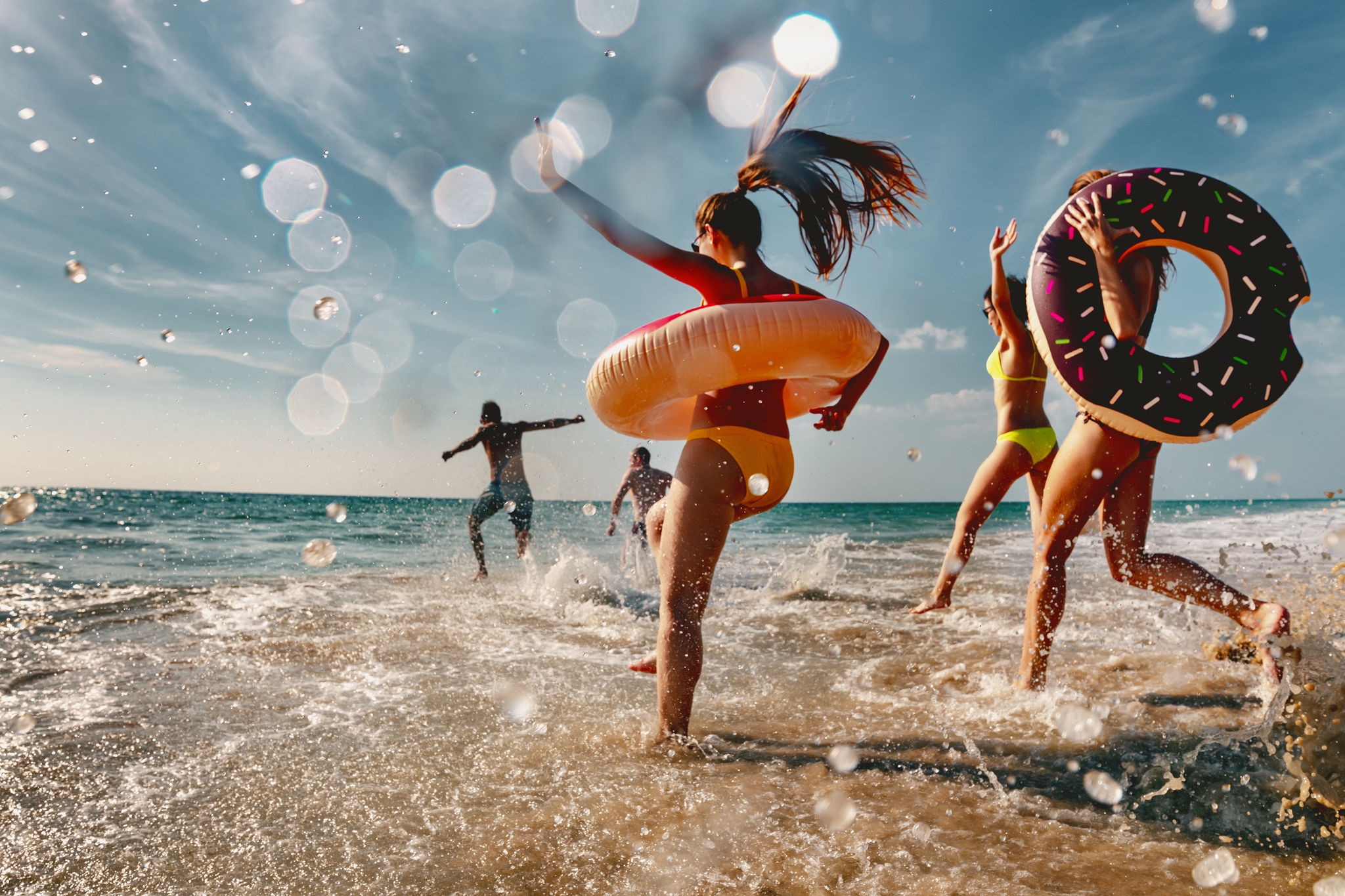 Old style photo of group of friends are having fun and running to sea beach with inflatable donuts