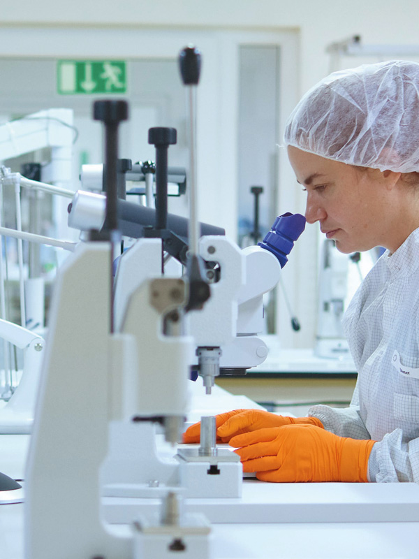 Pracownica ochrony zdrowia siedząca przy stole, analizująca próbki za pomocą mikroskopu medycznego