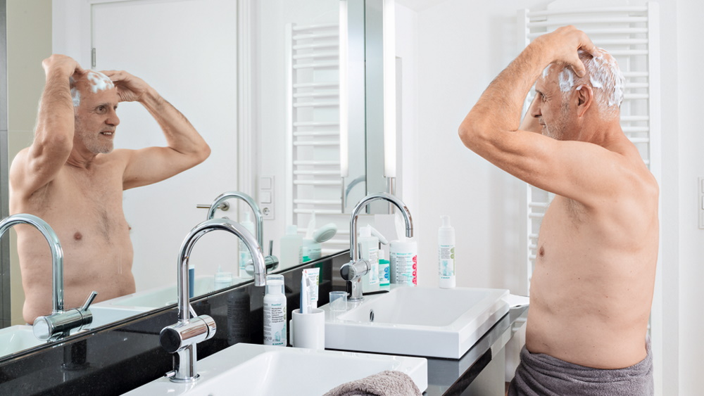 starszy mężczyzna wykonujący w domu antybakteryjne mycie włosów przed lustrem kąpielowym 