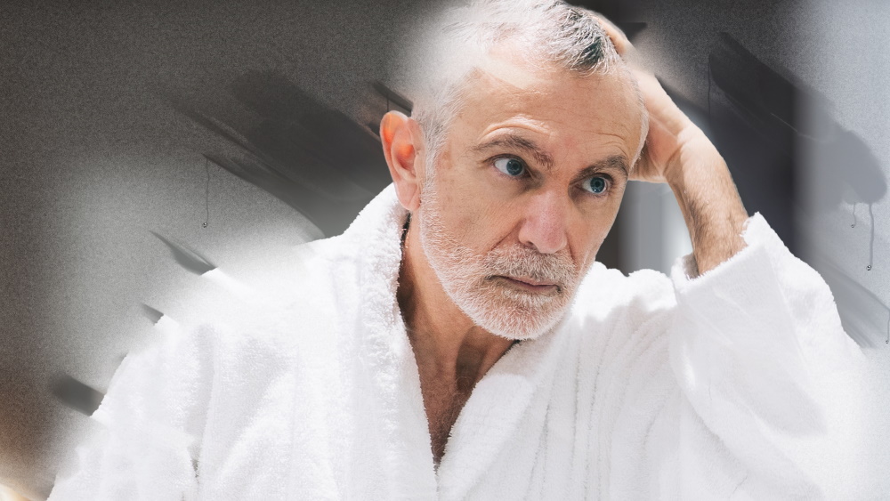 Starszy mężczyzna w szlafroku patrzy w zaparowane lusterko łazienkowe